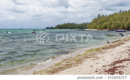 Small motorboat anchored in the shallow turquoise water near a sandy tropical beach at Ile aux Cerfs, Mauritius Small motorboat anchored in the shallow turquoise water near a sandy tropical beach at Ile aux Cerfs, Mauritius 141693257