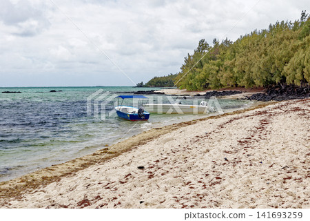 Small motorboat anchored in the shallow turquoise water near a sandy tropical beach at Ile aux Cerfs, Mauritius Small motorboat anchored in the shallow turquoise water near a sandy tropical beach at Ile aux Cerfs, Mauritius 141693259