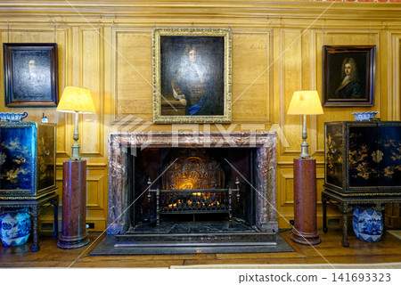 An antique marble fireplace with historical portraits and lacquer cabinets in the Great Hall at Dyrham Park, England An antique marble fireplace with historical portraits and lacquer cabinets in the Great Hall at Dyrham Park, England 141693323