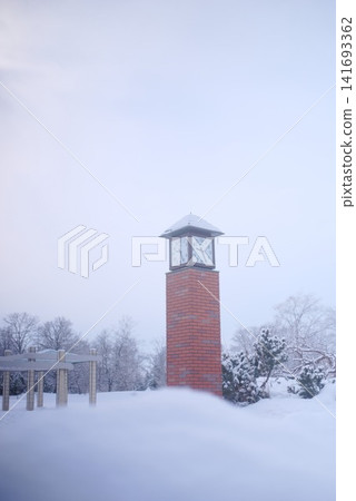 A brick clock tower stands in a snow-covered park, amidst a winter landscape. A brick clock tower stands in a snow-covered park, amidst a winter landscape. 141693362