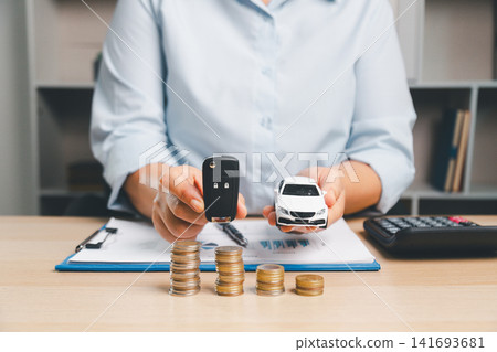 Business professional presenting car key and white toy car above coin stacks, representing vehicle ownership, car handover, auto loan approval, and transportation finance concept. 141693681