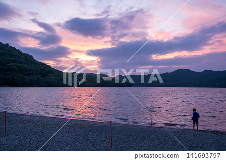 A child's back as they gaze at the fantastical sky by the lake at dusk. A child's back as they gaze at the fantastical sky by the lake at dusk. 141693797