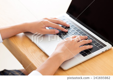 A middle school student in uniform opens a laptop at the living room table. A middle school student in uniform opens a laptop at the living room table. 141693862