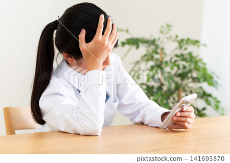 一名身穿校服的中學生坐在客廳的桌子旁,看著她的智慧型手機若有所思。 一名身穿校服的中學生坐在客廳的桌子旁,看著她的智慧型手機若有所思。 141693870