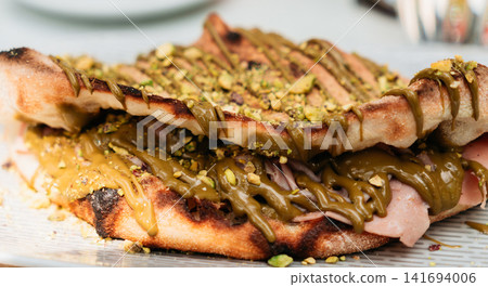 Artisan flatbread sandwich filled with savory meat and topped with pistachio cream and crushed nuts. Creative gourmet serving delivers a modern premium food concept Artisan flatbread sandwich filled with savory meat and topped with pistachio cream and crushed nuts. Creative gourmet serving delivers a modern premium food concept 141694006