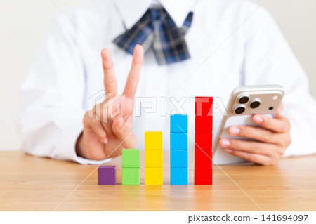 一名身穿校服的中學生女生手持智慧型手機和用彩色積木拼成的圖表,比出和平手勢。 一名身穿校服的中學生女生手持智慧型手機和用彩色積木拼成的圖表,比出和平手勢。 141694097