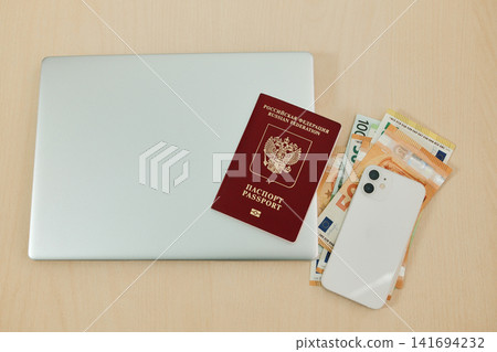 Russian passport lies on euro banknotes beside a laptop and smartphone on a desk. Concept of relocation from Russia, remote work setup and financial planning for moving abroad Russian passport lies on euro banknotes beside a laptop and smartphone on a desk. Concept of relocation from Russia, remote work setup and financial planning for moving abroad 141694232