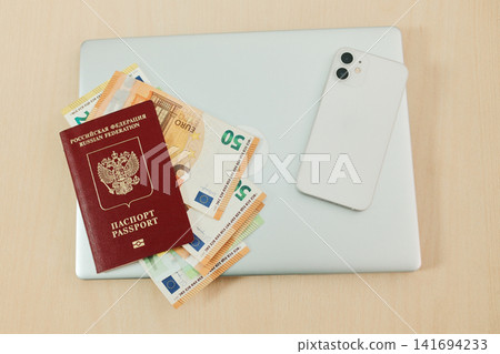 Laptop, Russian passport, euro banknotes and smartphone are arranged on a clean desk. Concept of relocation from Russia, remote work and financial planning for moving abroad Laptop, Russian passport, euro banknotes and smartphone are arranged on a clean desk. Concept of relocation from Russia, remote work and financial planning for moving abroad 141694233