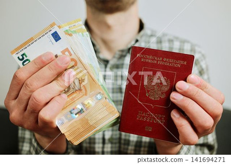 Hands hold a Russian passport with mixed euro banknotes in front of the body. Concept of relocation from Russia, migration budget and financial planning for moving abroad Hands hold a Russian passport with mixed euro banknotes in front of the body. Concept of relocation from Russia, migration budget and financial planning for moving abroad 141694271