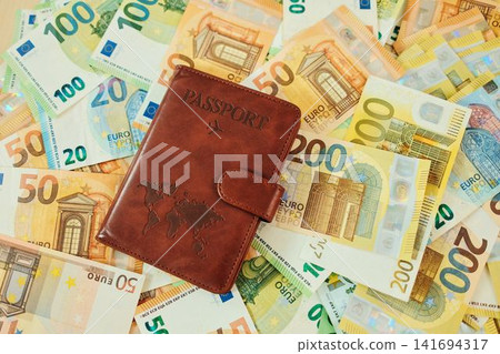 Brown passport wallet lies on scattered 20, 50, 100 and 200 euro banknotes. Travel budget concept with passport, European cash and vacation planning Brown passport wallet lies on scattered 20, 50, 100 and 200 euro banknotes. Travel budget concept with passport, European cash and vacation planning 141694317