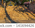Wide stone staircase with tree shadows and decorative fountain on a Mediterranean-style building exterior in evening light 141694426