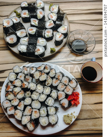 Homemade sushi rolls served on plates with soy sauce, wasabi and pickled ginger on wooden table. Traditional japanese food arrangement with fresh ingredients 141694707