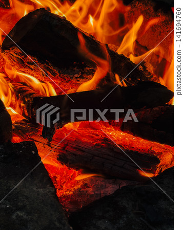 Glowing firewood burns with bright orange flames in close detail. Warm heat concept for fireplace, winter comfort, energy and natural fire texture Glowing firewood burns with bright orange flames in close detail. Warm heat concept for fireplace, winter comfort, energy and natural fire texture 141694760