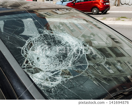 Broken windshield with heavy impact cracks parked on city street. Urban accident damage concept for insurance, transport risk, safety and vehicle repair 141694876