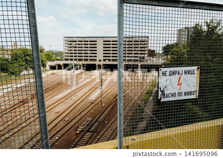 Warning sign with electric hazard message stands above railway tracks in Belgrade Serbia. Concept of transportation safety, danger and urban infrastructure Warning sign with electric hazard message stands above railway tracks in Belgrade Serbia. Concept of transportation safety, danger and urban infrastructure 141695096