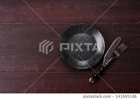 An empty round ceramic plate on a dark, textured brown background. An empty round plate An empty round ceramic plate on a dark, textured brown background. An empty round plate 141695186