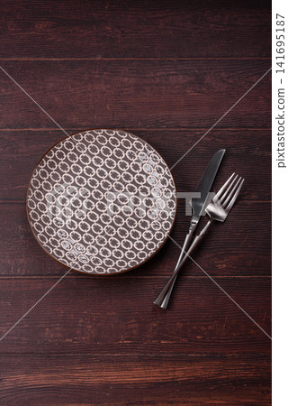 An empty round ceramic plate on a dark, textured brown background. An empty round plate An empty round ceramic plate on a dark, textured brown background. An empty round plate 141695187