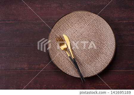 An empty round ceramic plate on a dark, textured brown background. An empty round plate An empty round ceramic plate on a dark, textured brown background. An empty round plate 141695189