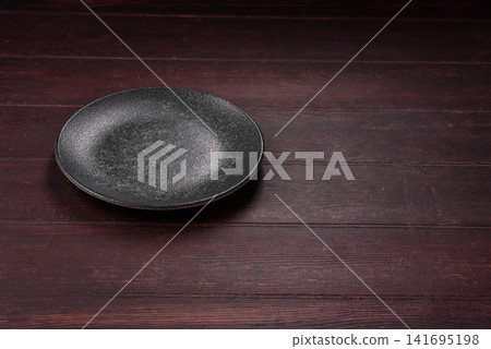 An empty round ceramic plate on a dark, textured brown background. An empty round plate An empty round ceramic plate on a dark, textured brown background. An empty round plate 141695198