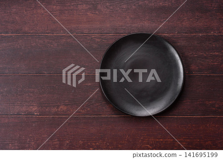 An empty round ceramic plate on a dark, textured brown background. An empty round plate An empty round ceramic plate on a dark, textured brown background. An empty round plate 141695199