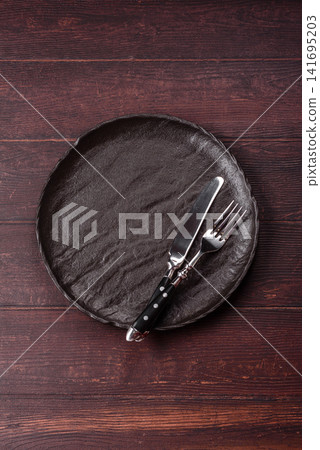 An empty round ceramic plate on a dark, textured brown background. An empty round plate An empty round ceramic plate on a dark, textured brown background. An empty round plate 141695203
