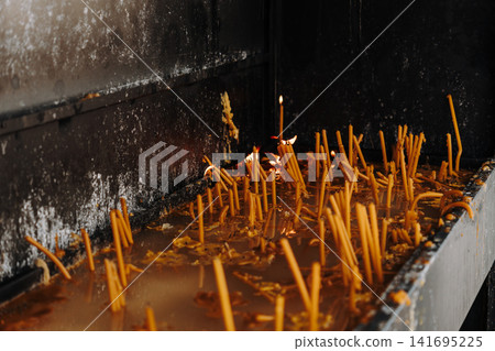 Burning candles glow inside a blackened religious shrine. Concept of faith, remembrance, spirituality and peaceful reflection Burning candles glow inside a blackened religious shrine. Concept of faith, remembrance, spirituality and peaceful reflection 141695225