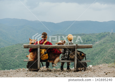 Couple of travelers sitting with two dogs German and Australian Shepherd on a mountain bench in Serbia. Rear back view. Concept of friendship, hiking and outdoor lifestyle Couple of travelers sitting with two dogs German and Australian Shepherd on a mountain bench in Serbia. Rear back view. Concept of friendship, hiking and outdoor lifestyle 141695240