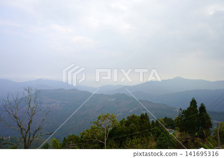 Scenic wide landscape view of layered green mountains under a hazy cloudy sky 141695316