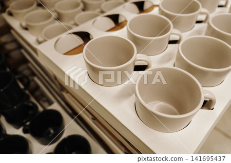 Minimal white ceramic cups arranged in a retail display for modern kitchen and dining concepts. Clean household and cafe interior aesthetic Minimal white ceramic cups arranged in a retail display for modern kitchen and dining concepts. Clean household and cafe interior aesthetic 141695437