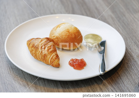 A plate featuring fragrant croissants and rolls served with jam and butter. A plate featuring fragrant croissants and rolls served with jam and butter. 141695860