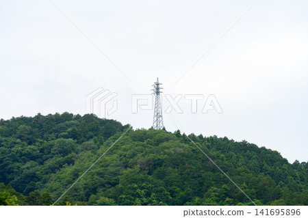 A power transmission tower stands atop a lush green mountain. A power transmission tower stands atop a lush green mountain. 141695896