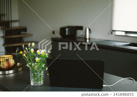 Laptop on a dark kitchen island with wildflowers in a glass vase inside a modern home. Remote work, hybrid workplace, work from home lifestyle. Laptop on a dark kitchen island with wildflowers in a glass vase inside a modern home. Remote work, hybrid workplace, work from home lifestyle. 141696855