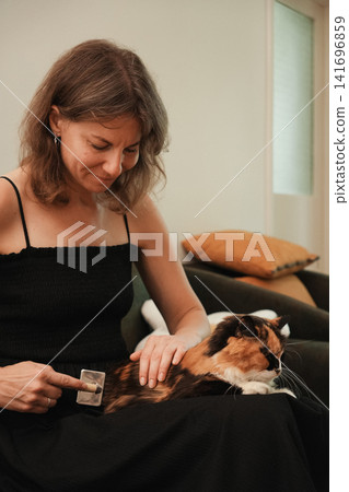 Woman carefully brushing a calm long haired calico cat while it rests on her lap. Warm home lifestyle scene promoting regular grooming, hygiene, and responsible pet ownership Woman carefully brushing a calm long haired calico cat while it rests on her lap. Warm home lifestyle scene promoting regular grooming, hygiene, and responsible pet ownership 141696859