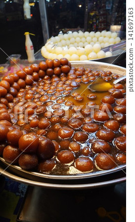 Rich gulab jamun glisten in syrup with spoon in serving dish, sweet dessert concept Rich gulab jamun glisten in syrup with spoon in serving dish, sweet dessert concept 141697163