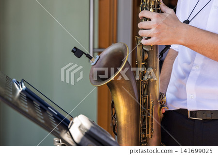 Musician playing a patinated tenor saxophone beside a black music stand Musician playing a patinated tenor saxophone beside a black music stand 141699025