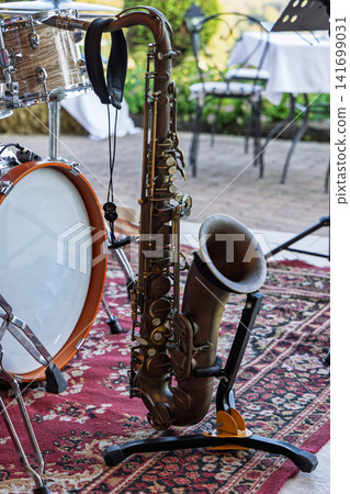 Tenor saxophone on a stand beside an acoustic drum kit on a garden patio Tenor saxophone on a stand beside an acoustic drum kit on a garden patio 141699031