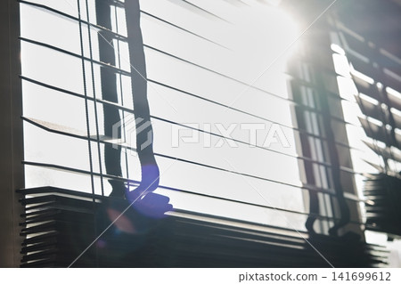 Low-angle view of horizontal wooden venetian window blinds against bright backlighting and lens flare. Sunlight streams directly through the open slats, creating a warm and bright ambiance Low-angle view of horizontal wooden venetian window blinds against bright backlighting and lens flare. Sunlight streams directly through the open slats, creating a warm and bright ambiance 141699612
