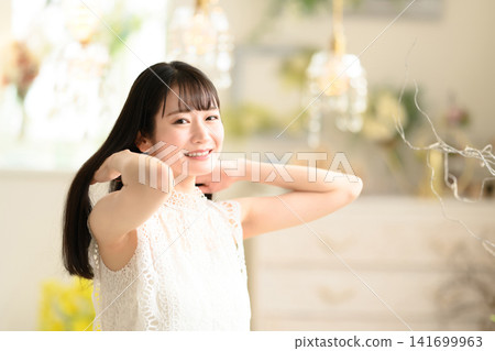 A woman in a white dress touches her hair with a smile. A woman in a white dress touches her hair with a smile. 141699963
