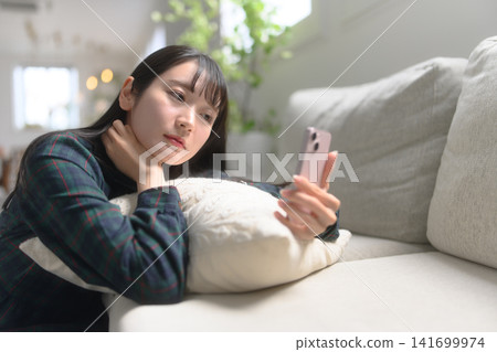 觀看在沙發的婦女一個智能手機 141699974