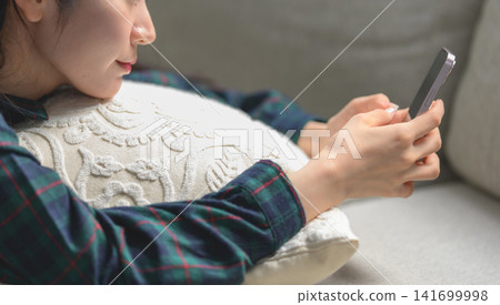 觀看在沙發的婦女一個智能手機 觀看在沙發的婦女一個智能手機 141699998