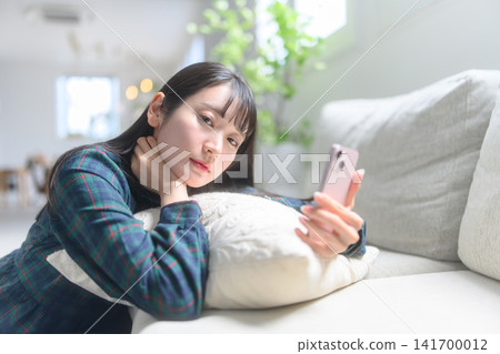 一個女人在沙發上操作智能手機 一個女人在沙發上操作智能手機 141700012