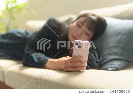 A woman engrossed in her smartphone screen while sitting on a sofa. 141700020