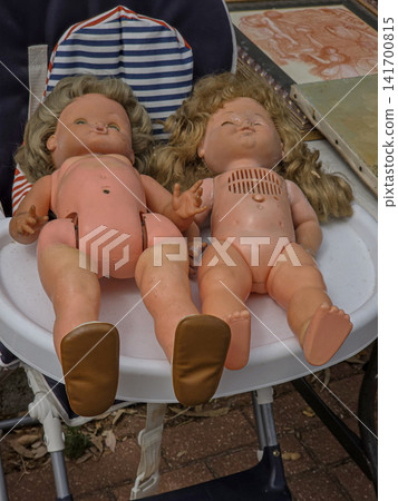 Worn retro plastic baby dolls resting together on a high chair at a flea market on a sunny day 141700815