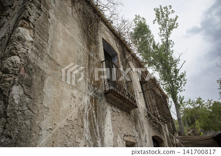 Old abandoned mansion facade shows rusted balcony and distressed walls in a quiet location Old abandoned mansion facade shows rusted balcony and distressed walls in a quiet location 141700817