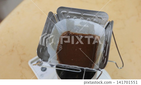 Close-up of freshly ground coffee blooming in a white paper filter inside a stainless steel pour-over dripper. Dark, rich coffee grounds are saturated with hot water, creating a bubbling surface durin Close-up of freshly ground coffee blooming in a white paper filter inside a stainless steel pour-over dripper. Dark, rich coffee grounds are saturated with hot water, creating a bubbling surface durin 141701551
