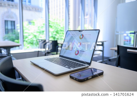 A laptop on an office desk with a view of greenery outside the window. A laptop on an office desk with a view of greenery outside the window. 141701624