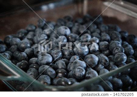 Close-up shot of fresh, ripe blueberries packed inside a clear glass baking dish. The berries display a natural light blue bloom coating, providing a vibrant texture for healthy eating Close-up shot of fresh, ripe blueberries packed inside a clear glass baking dish. The berries display a natural light blue bloom coating, providing a vibrant texture for healthy eating 141702205