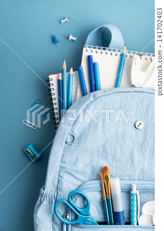 Blue backpack overflowing with school supplies including pencils notebooks and scissors on a blue background Blue backpack overflowing with school supplies including pencils notebooks and scissors on a blue background 141702403