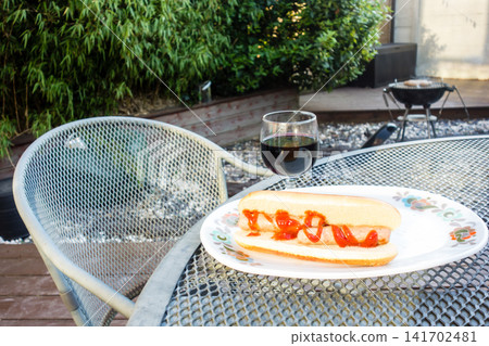 Hot dogs with sausages grilled over a barbecue and a glass of red wine – a barbecue dinner enjoyed in the garden. Hot dogs with sausages grilled over a barbecue and a glass of red wine – a barbecue dinner enjoyed in the garden. 141702481