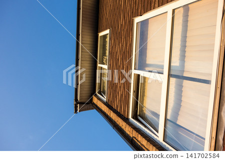 A brick building with large windows bathed in the setting sun under a clear blue sky - a house in the suburbs of London, England. A brick building with large windows bathed in the setting sun under a clear blue sky - a house in the suburbs of London, England. 141702584